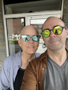 The two of us in front of what would have been the door to The Jabberwocky. Older white male and female looking at the camera, both in sunglasses.