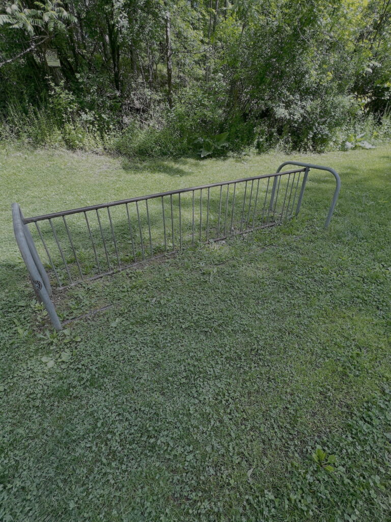 Photograph of an old-style steel tubular bicycle rack, sitting on an open lawn area.